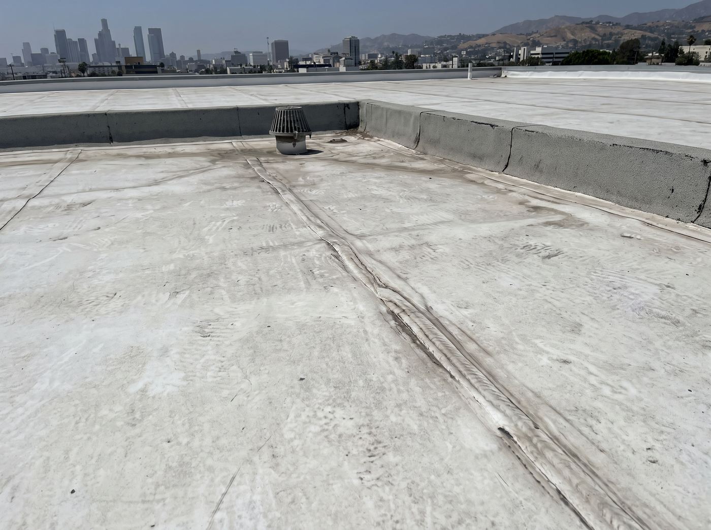 A heat-welded seam on a white TPO membrane beside a roof drain